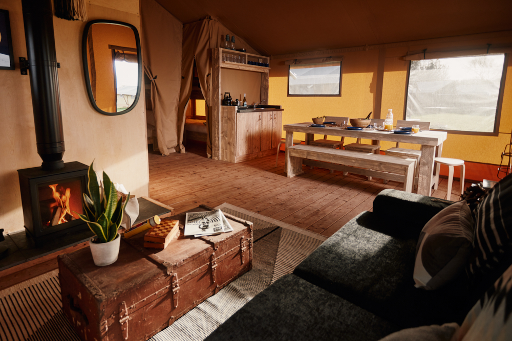 
								Living area, wood burner, dinning table and kitchen in the glamping safari tent at The Camp at The Wave great campsite for UK holidays							